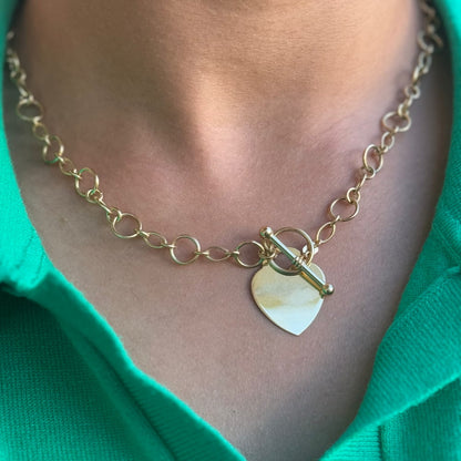 close up of a women wearing a gold necklace with heart pendant and a toggle clasp