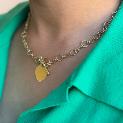 close up of a woman wearing a gold necklace with heart pendant and a toggle clasp